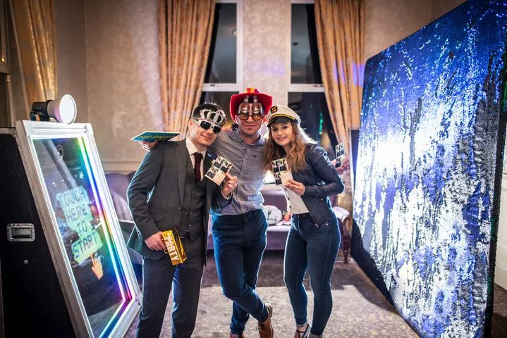 Three friends posing with printed photos and props at the Magic Mirror photo booth, all smiling and having fun.